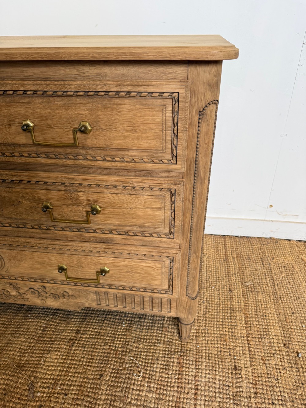 A rectangular scrubbed oak commode featuring three drawers with brass handles and subtle classical carved detailing on the facade. View II