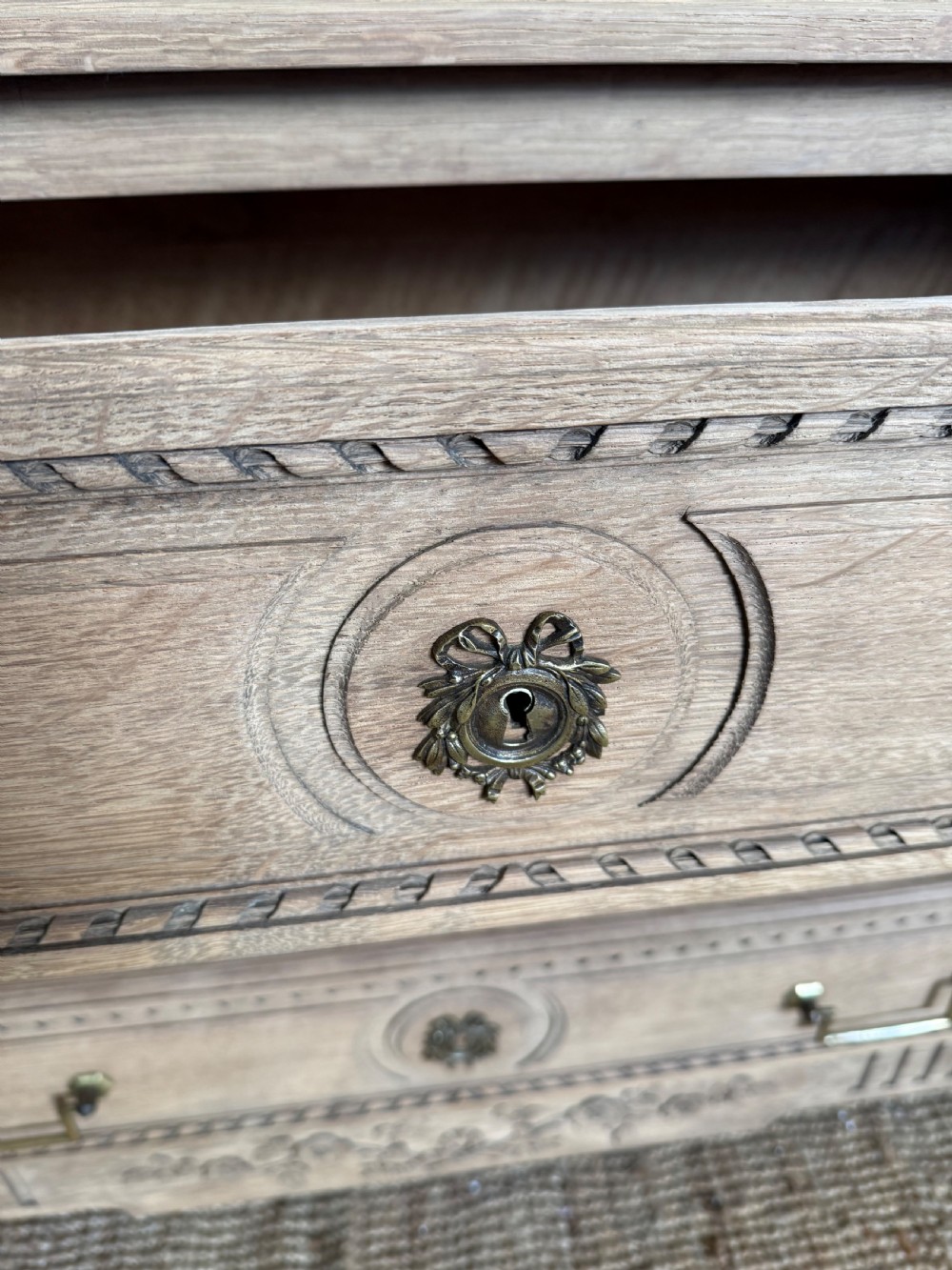 A rectangular scrubbed oak commode featuring three drawers with brass handles and subtle classical carved detailing on the facade. View XI