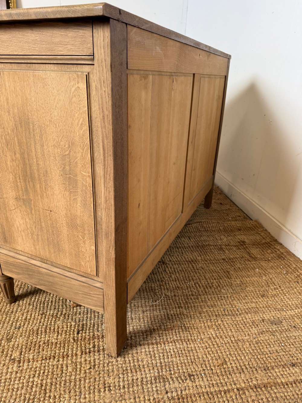 A rectangular scrubbed oak commode featuring three drawers with brass handles and subtle classical carved detailing on the facade. View XII