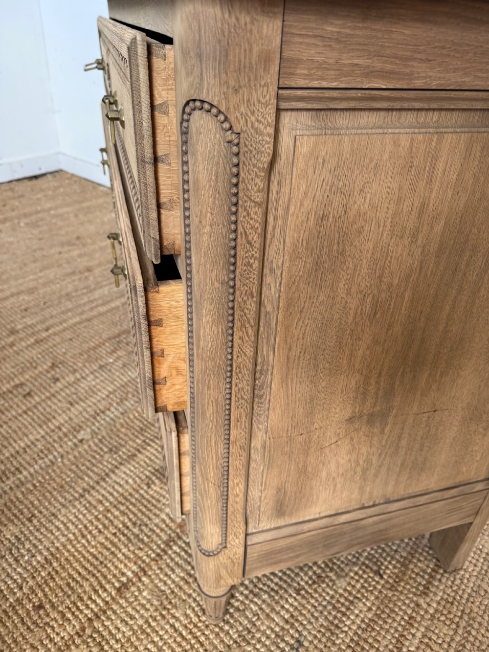A rectangular scrubbed oak commode featuring three drawers with brass handles and subtle classical carved detailing on the facade. View XIV