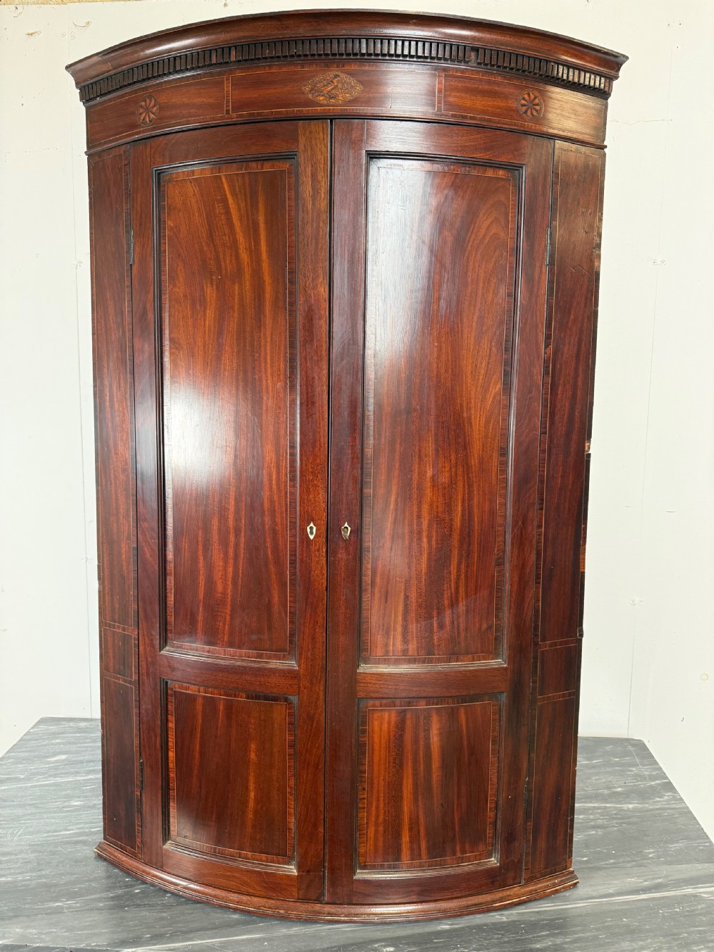 A Georgian mahogany bow-fronted corner cupboard featuring curved twin panelled doors, dentil moulding, and central marquetry inlay. View II