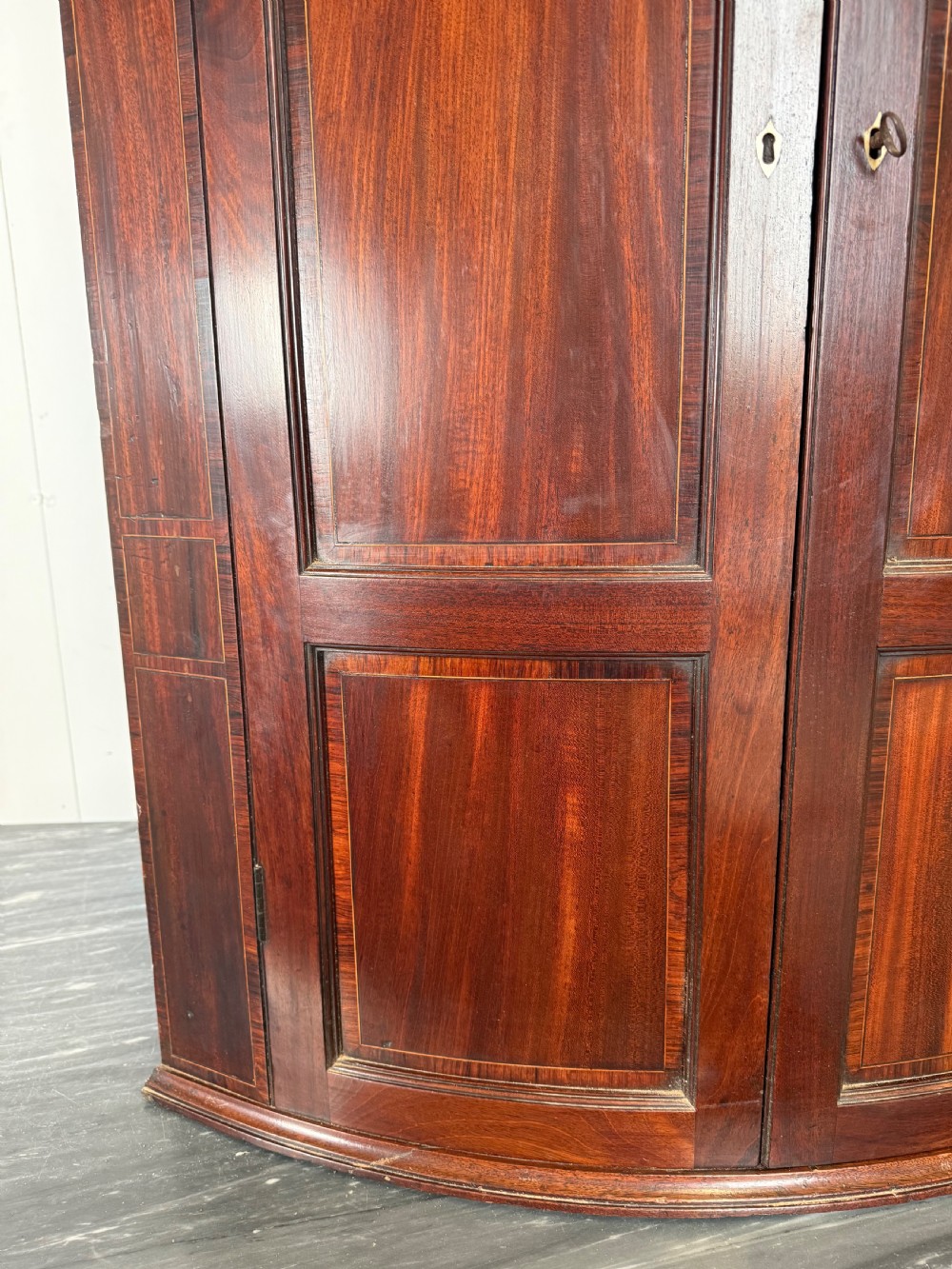 A Georgian mahogany bow-fronted corner cupboard featuring curved twin panelled doors, dentil moulding, and central marquetry inlay. View III