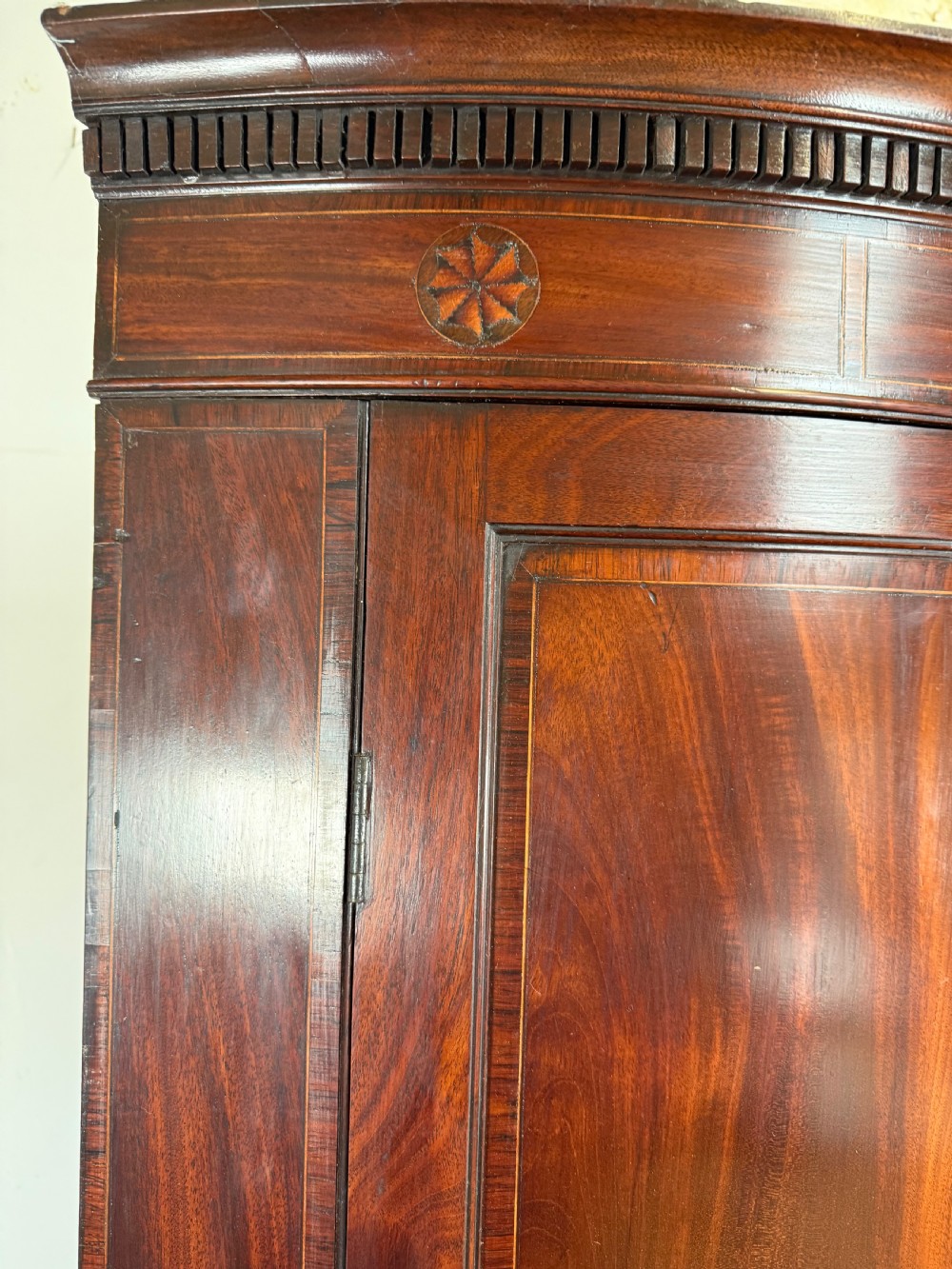 A Georgian mahogany bow-fronted corner cupboard featuring curved twin panelled doors, dentil moulding, and central marquetry inlay. View IV