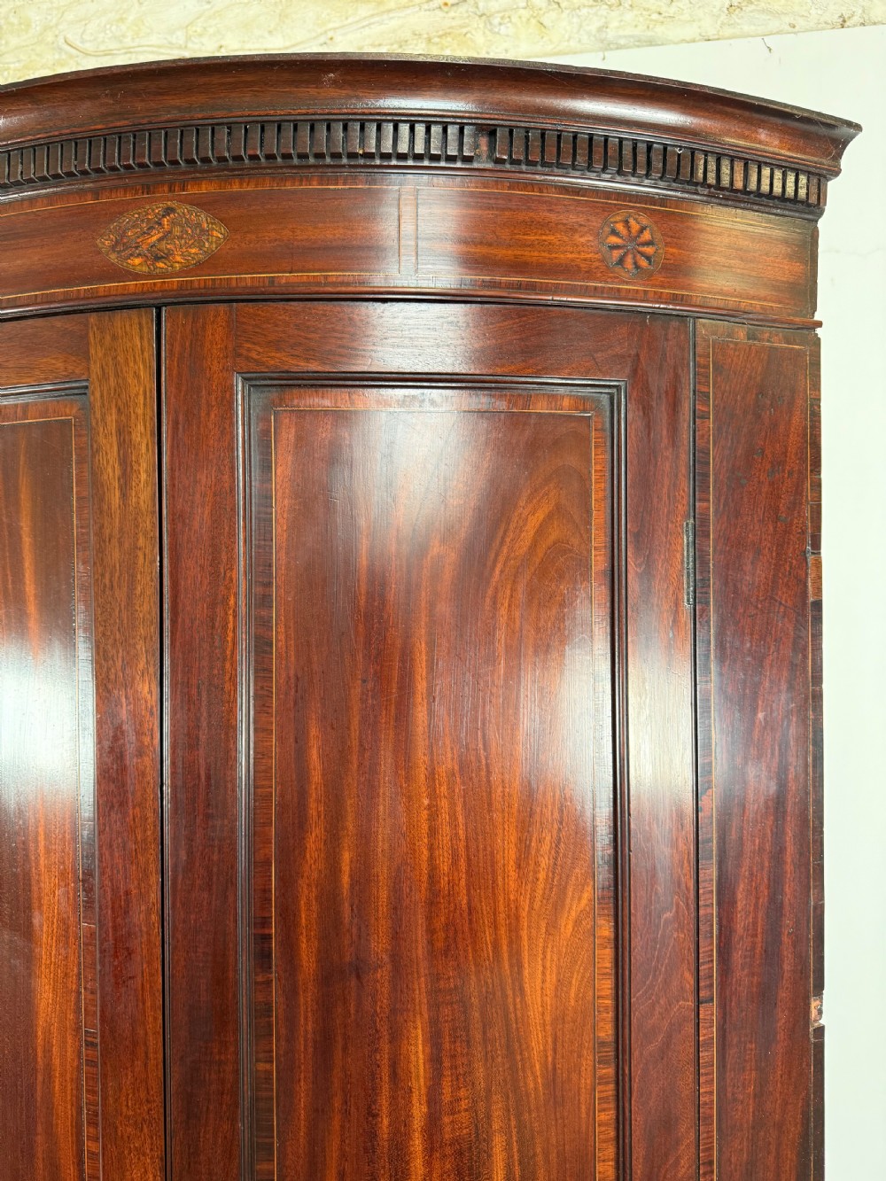 A Georgian mahogany bow-fronted corner cupboard featuring curved twin panelled doors, dentil moulding, and central marquetry inlay. View VI