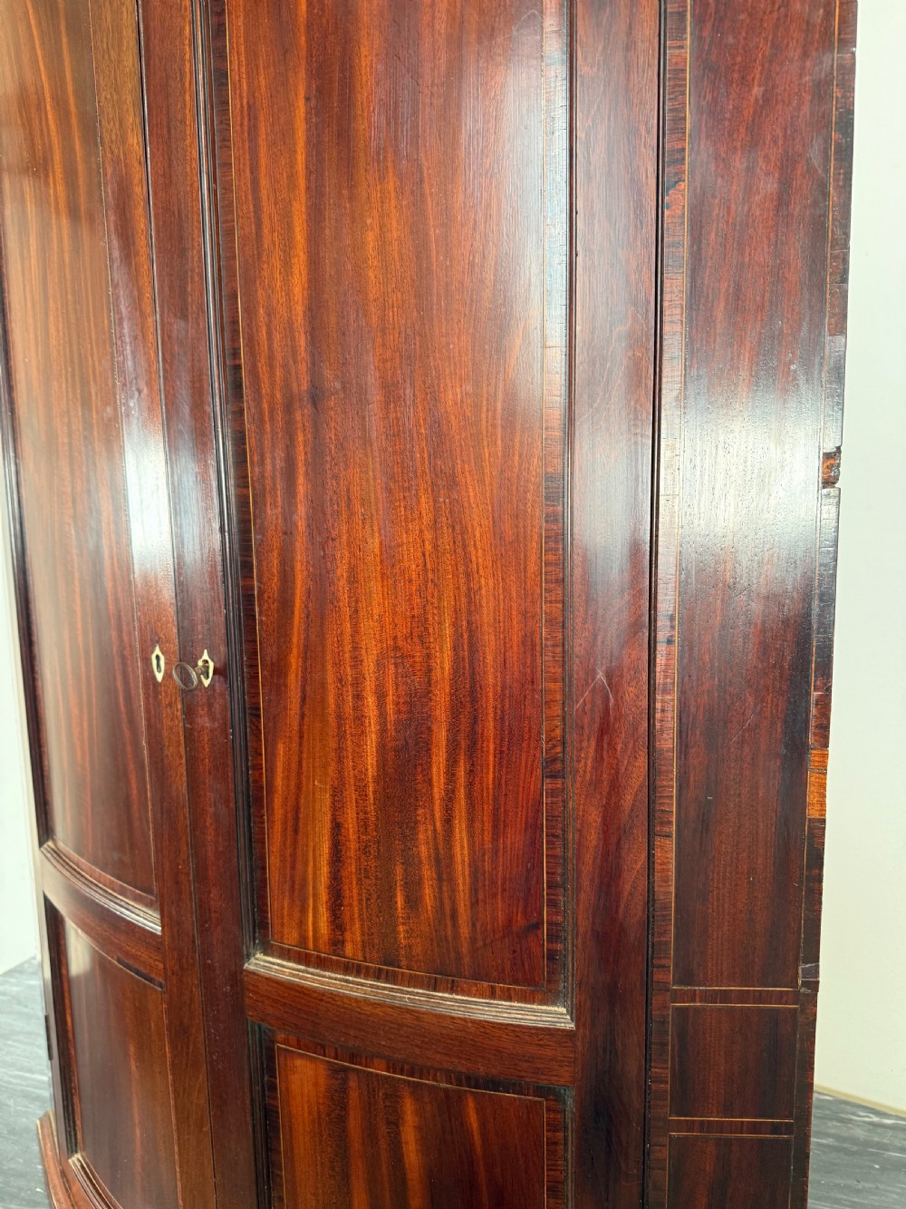 A Georgian mahogany bow-fronted corner cupboard featuring curved twin panelled doors, dentil moulding, and central marquetry inlay. View VII