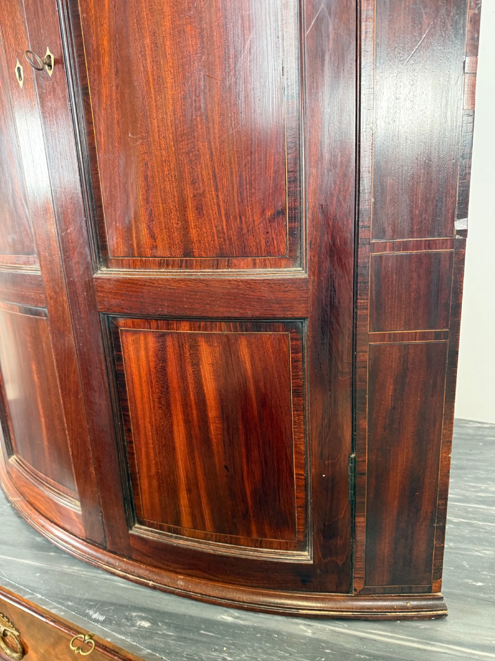 A Georgian mahogany bow-fronted corner cupboard featuring curved twin panelled doors, dentil moulding, and central marquetry inlay. View VIII