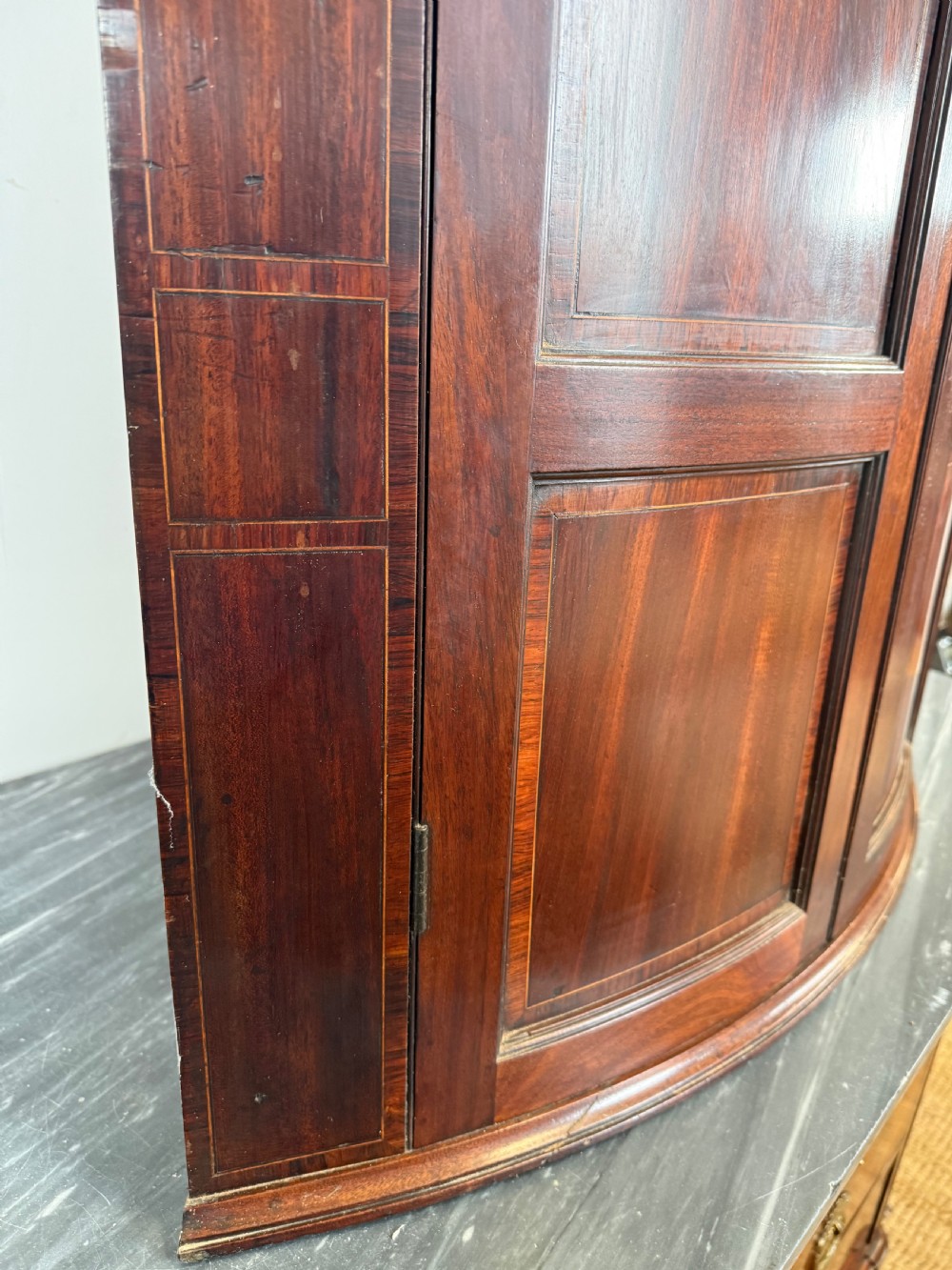 A Georgian mahogany bow-fronted corner cupboard featuring curved twin panelled doors, dentil moulding, and central marquetry inlay. View IX