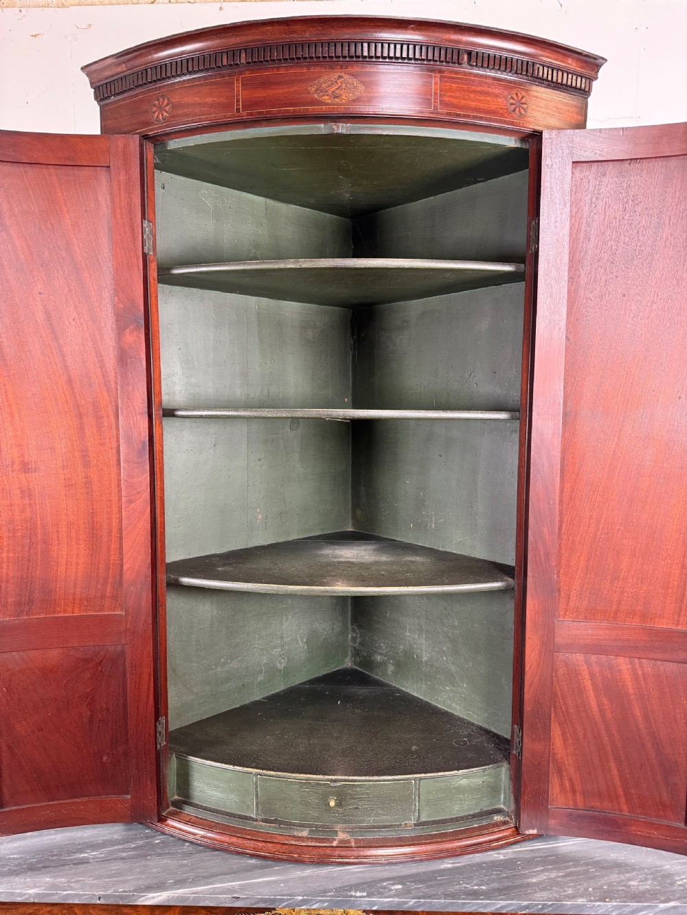 A Georgian mahogany bow-fronted corner cupboard featuring curved twin panelled doors, dentil moulding, and central marquetry inlay. View X