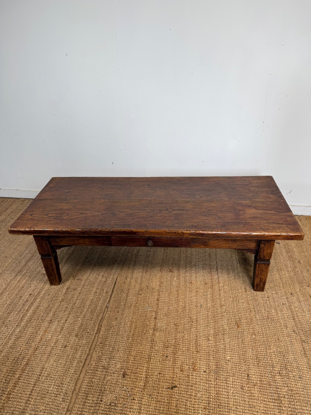 A low rectangular 19th-century dark elm coffee table featuring a wide plank top, central apron drawer with a round wooden knob, and four square legs.