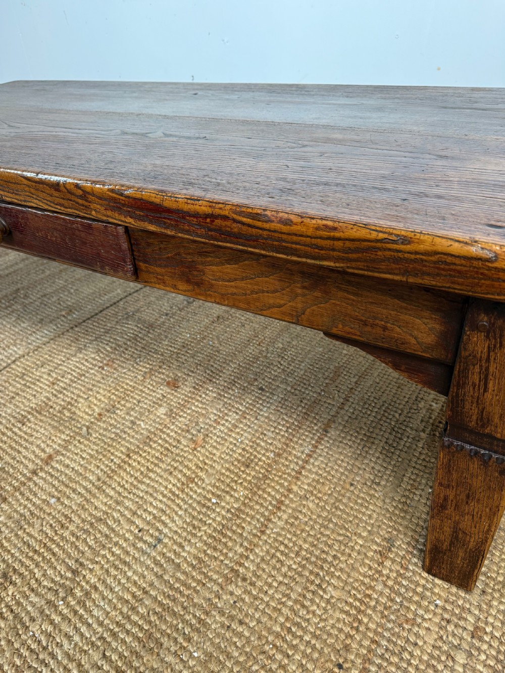 A low rectangular 19th-century dark elm coffee table featuring a wide plank top, central apron drawer with a round wooden knob, and four square legs. View V