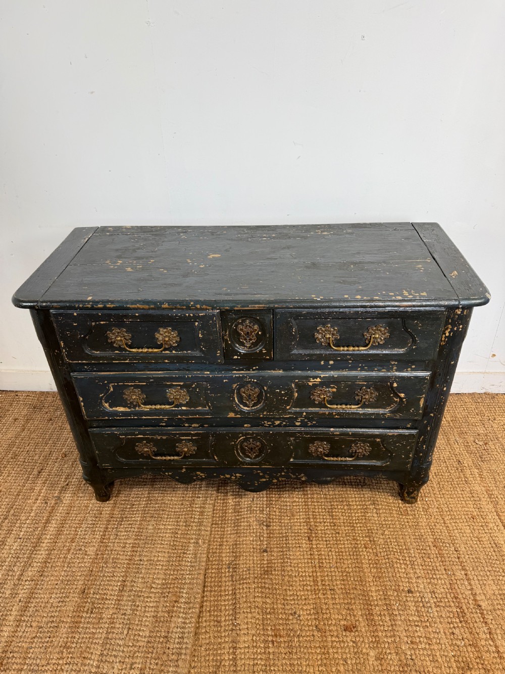 An antique dark-painted French commode featuring three rows of drawers with distressed black paint revealing bare wood underneath and decorative brass hardware.