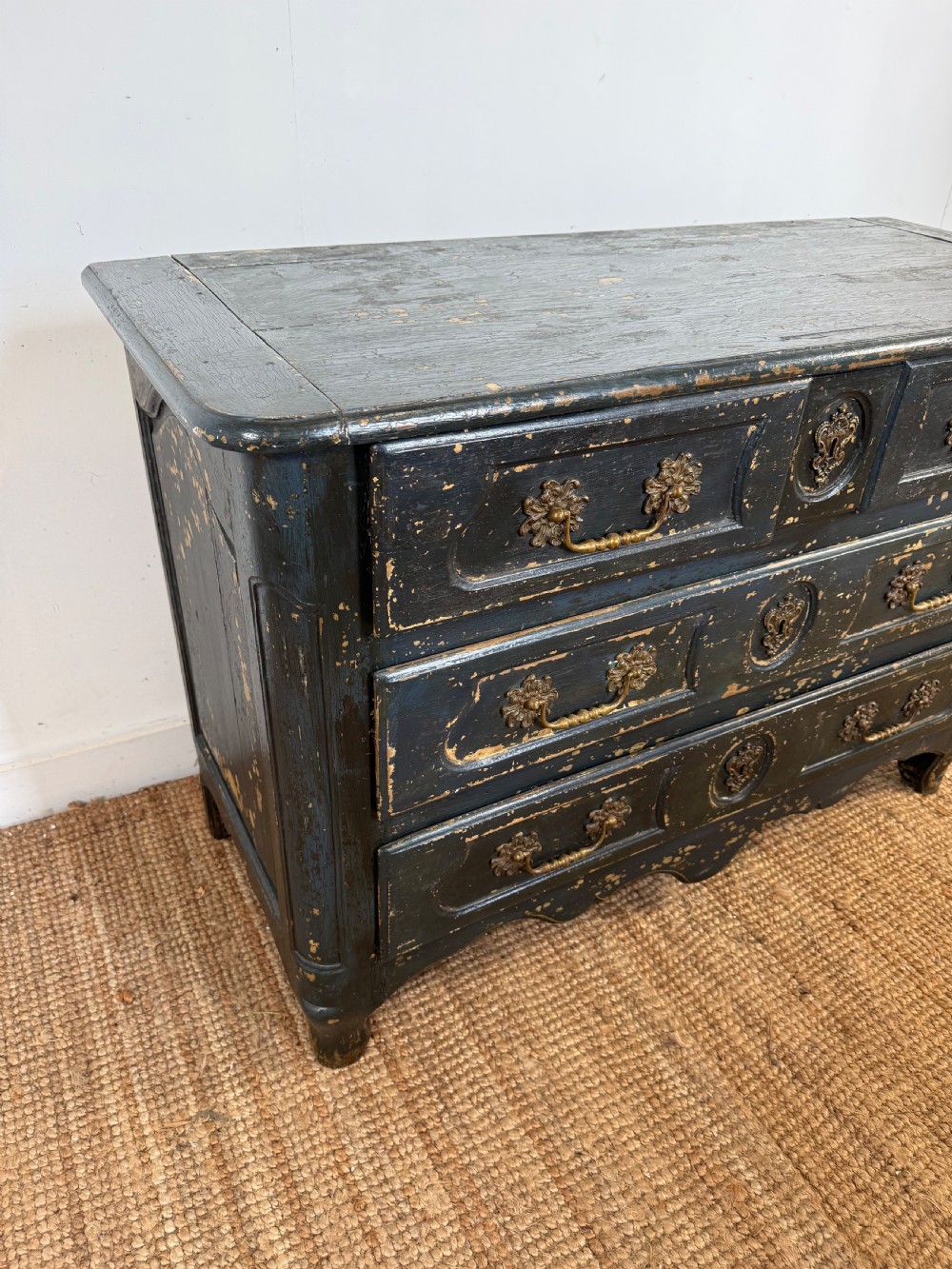 An antique dark-painted French commode featuring three rows of drawers with distressed black paint revealing bare wood underneath and decorative brass hardware. View II