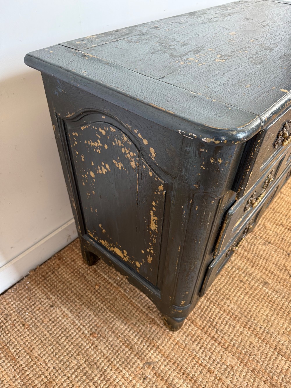 An antique dark-painted French commode featuring three rows of drawers with distressed black paint revealing bare wood underneath and decorative brass hardware. View III