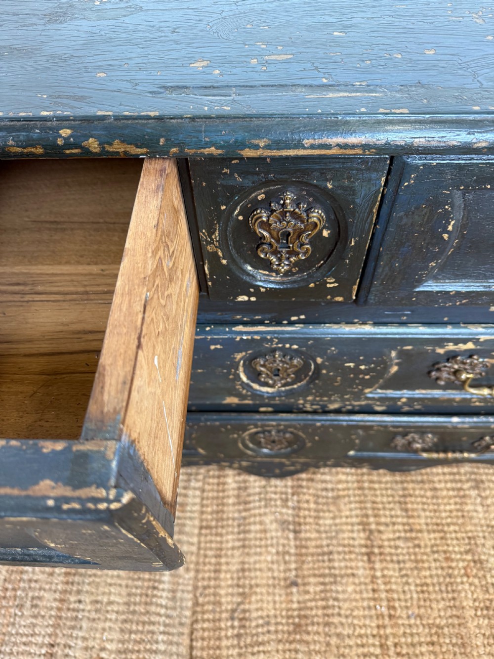 An antique dark-painted French commode featuring three rows of drawers with distressed black paint revealing bare wood underneath and decorative brass hardware. View VIII