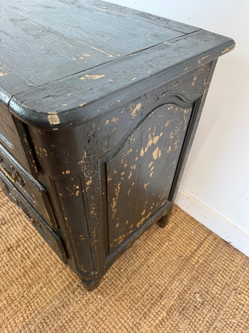 An antique dark-painted French commode featuring three rows of drawers with distressed black paint revealing bare wood underneath and decorative brass hardware. View IX