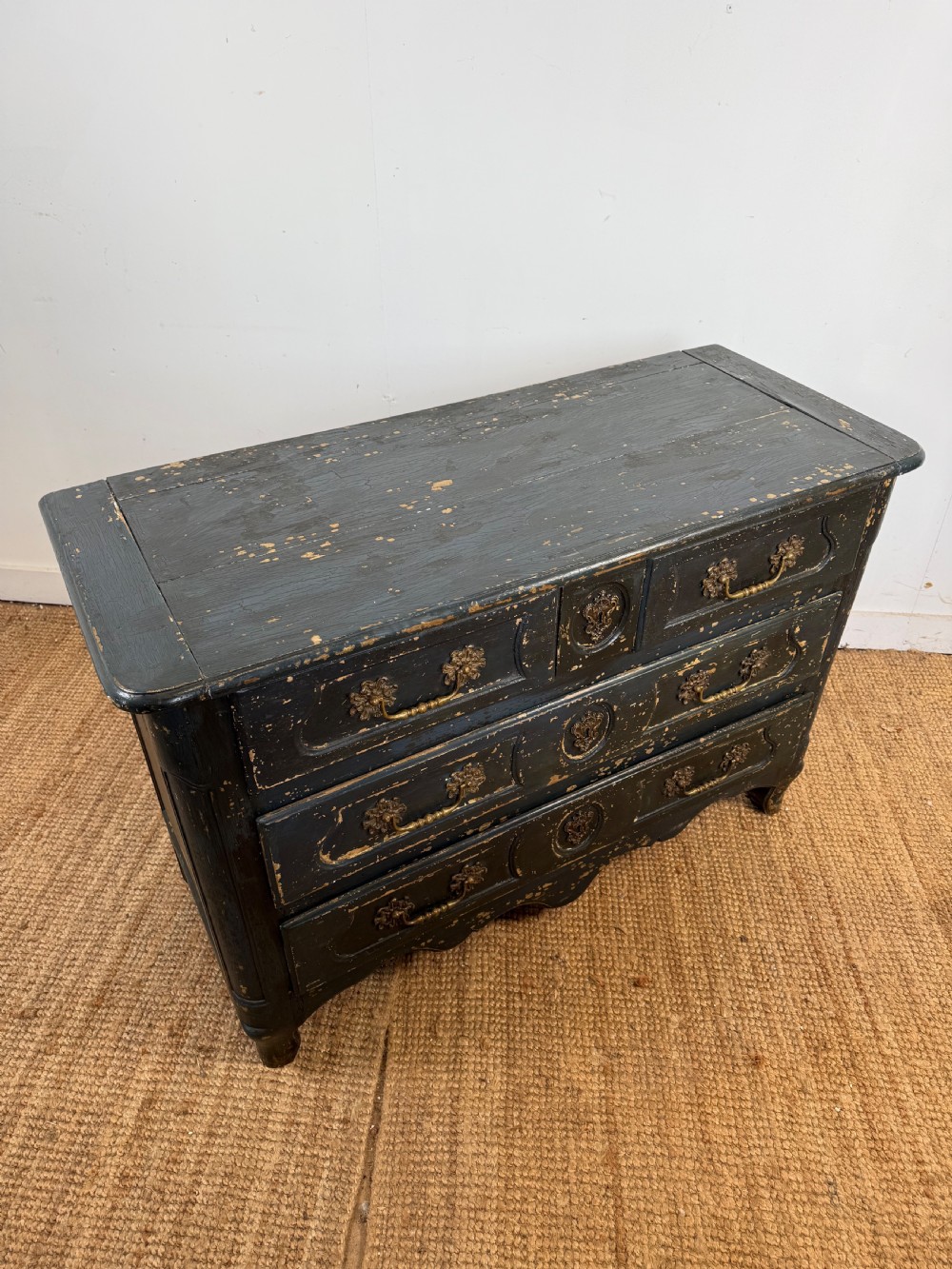 An antique dark-painted French commode featuring three rows of drawers with distressed black paint revealing bare wood underneath and decorative brass hardware. View X