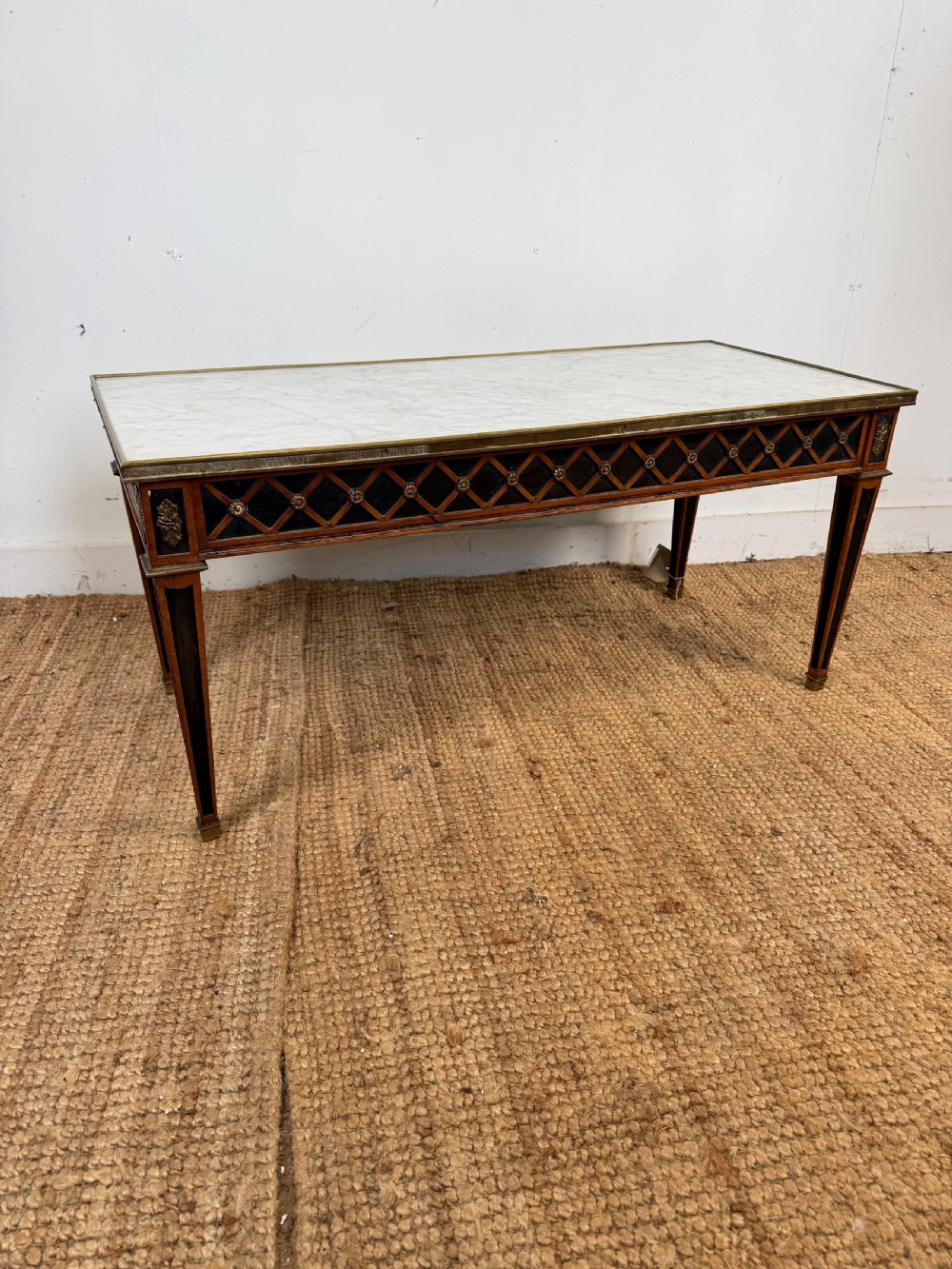 A rectangular Louis XVI style coffee table with a white marble top, dark wood lattice frieze, metal mounts, and tapered square legs.