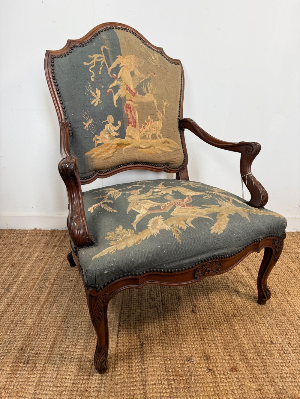 A late 19th-century open armchair with a carved walnut frame, cabriole legs, and muted green tapestry upholstery featuring pictorial motifs.