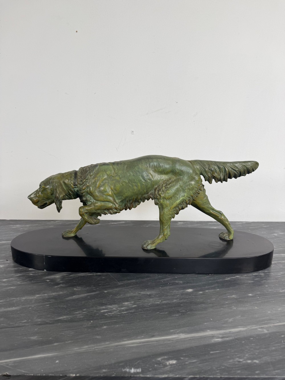 An Art Deco spelter sculpture depicting a prowling hunting dog with a green verdigris patina finish, mounted on an oval black marble base.