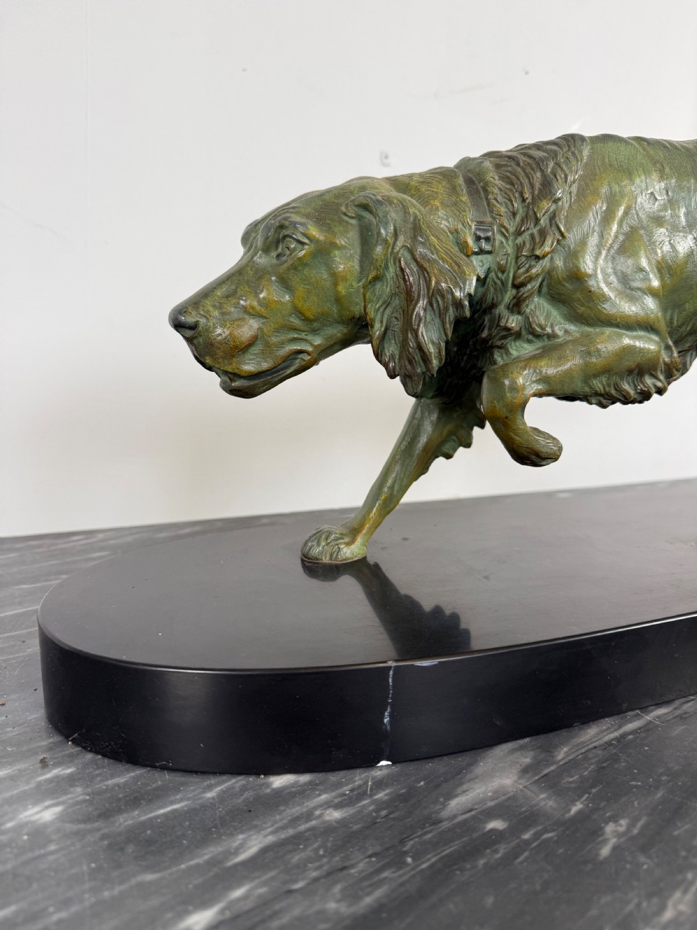 An Art Deco spelter sculpture depicting a prowling hunting dog with a green verdigris patina finish, mounted on an oval black marble base. View II