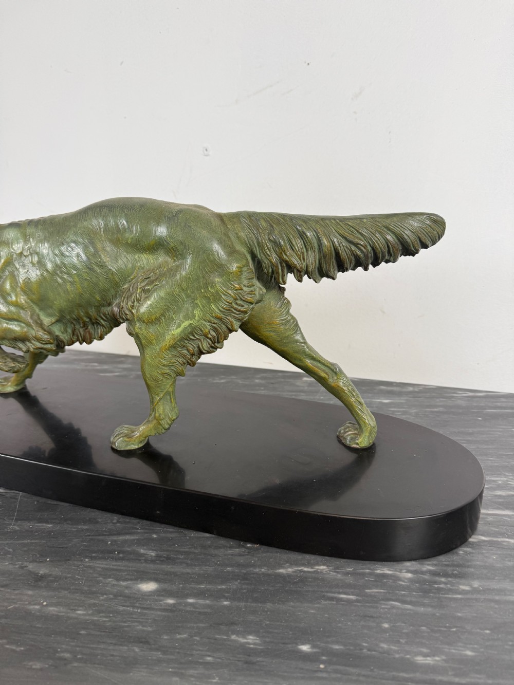 An Art Deco spelter sculpture depicting a prowling hunting dog with a green verdigris patina finish, mounted on an oval black marble base. View V