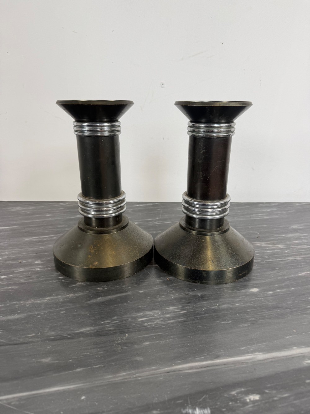 A pair of dark patinated metal Art Deco candlesticks featuring cylindrical columns, flared conical bases, and polished chrome ribbed bands.