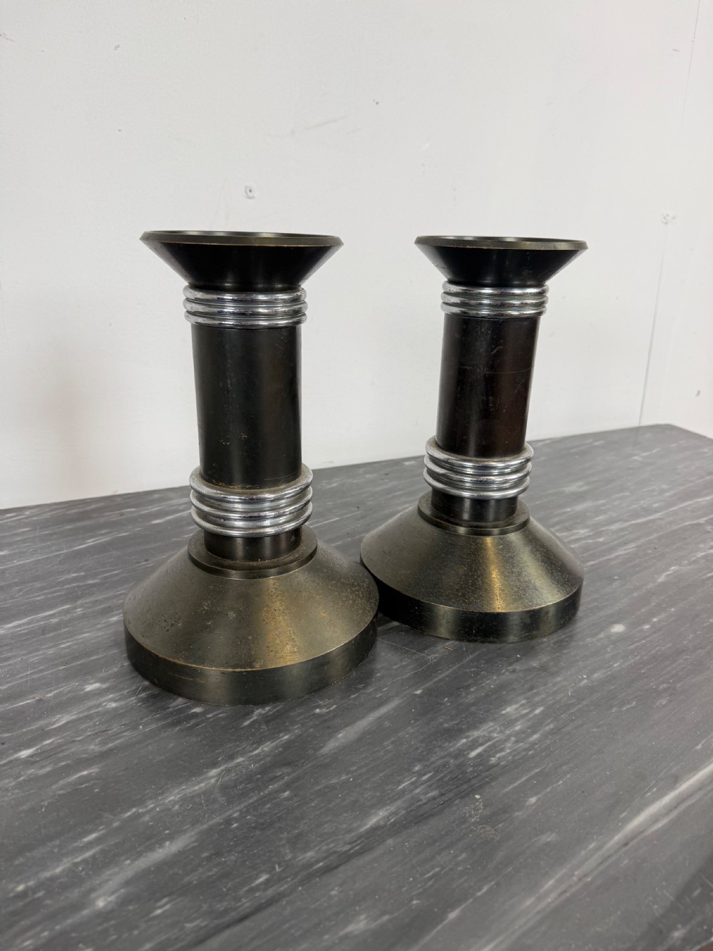 A pair of dark patinated metal Art Deco candlesticks featuring cylindrical columns, flared conical bases, and polished chrome ribbed bands. View II