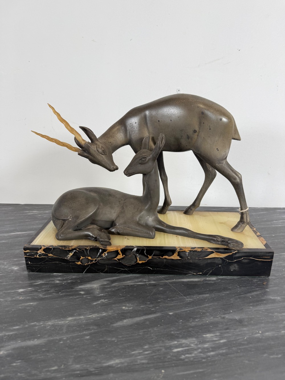 An Art Deco spelter sculpture featuring one standing horned deer and one reclining deer mounted on a rectangular black marble and amber onyx base.