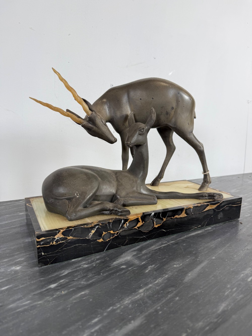 An Art Deco spelter sculpture featuring one standing horned deer and one reclining deer mounted on a rectangular black marble and amber onyx base. View II