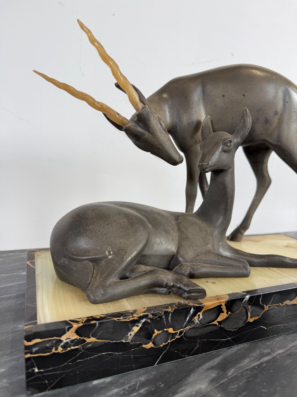 An Art Deco spelter sculpture featuring one standing horned deer and one reclining deer mounted on a rectangular black marble and amber onyx base. View III
