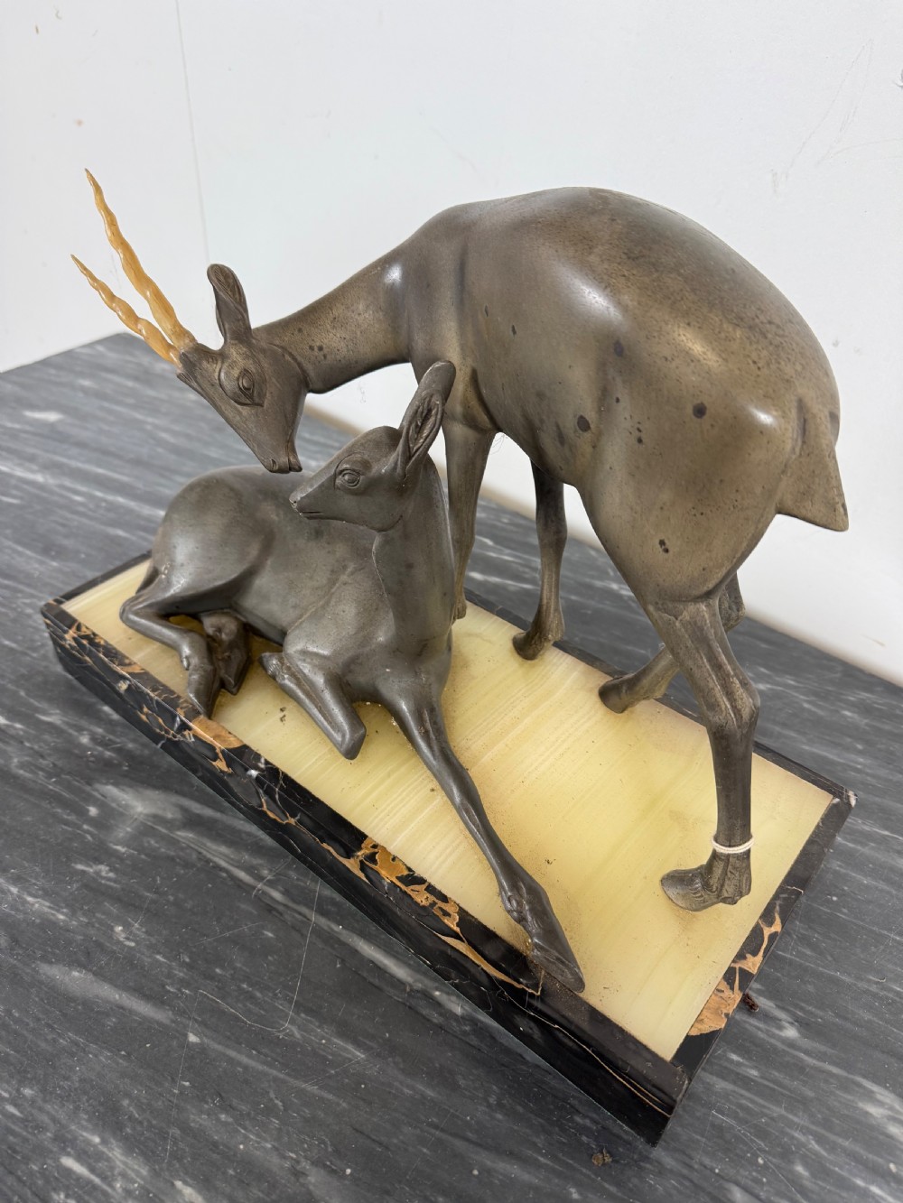 An Art Deco spelter sculpture featuring one standing horned deer and one reclining deer mounted on a rectangular black marble and amber onyx base. View V