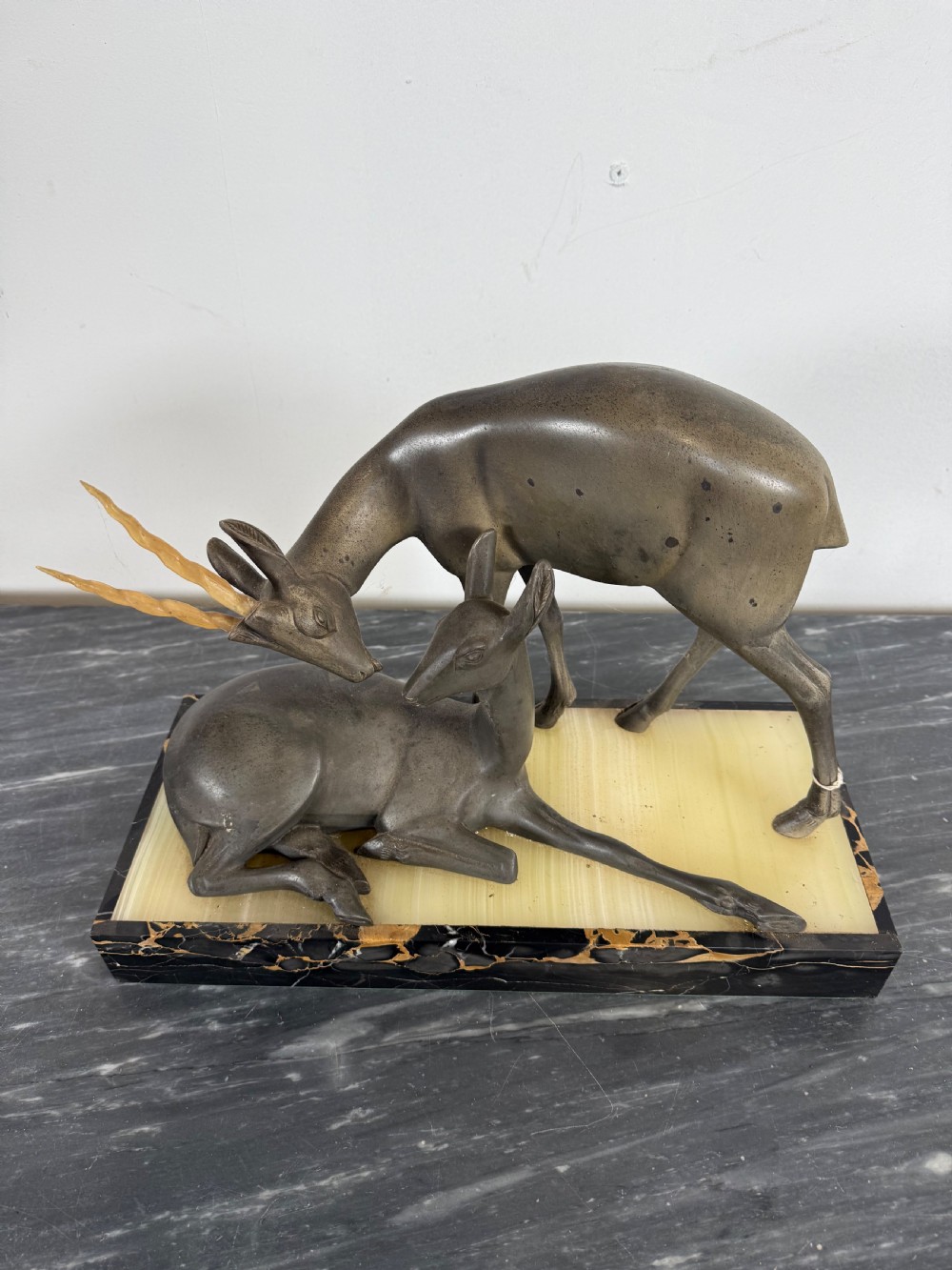 An Art Deco spelter sculpture featuring one standing horned deer and one reclining deer mounted on a rectangular black marble and amber onyx base. View VI