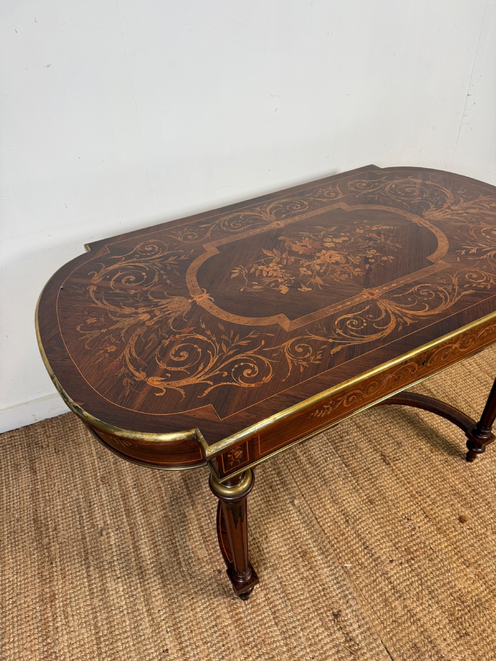 A French Napoleon III period centre table featuring floral wood marquetry, brass edges, tapered fluted legs, and an arched lower stretcher. View II