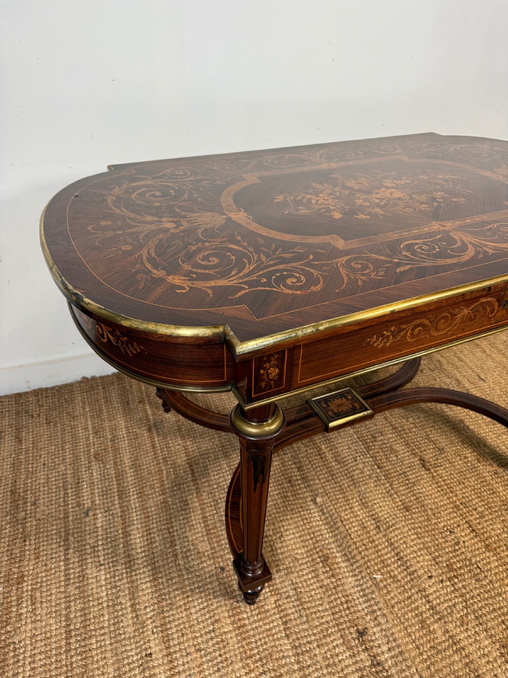 A French Napoleon III period centre table featuring floral wood marquetry, brass edges, tapered fluted legs, and an arched lower stretcher. View III
