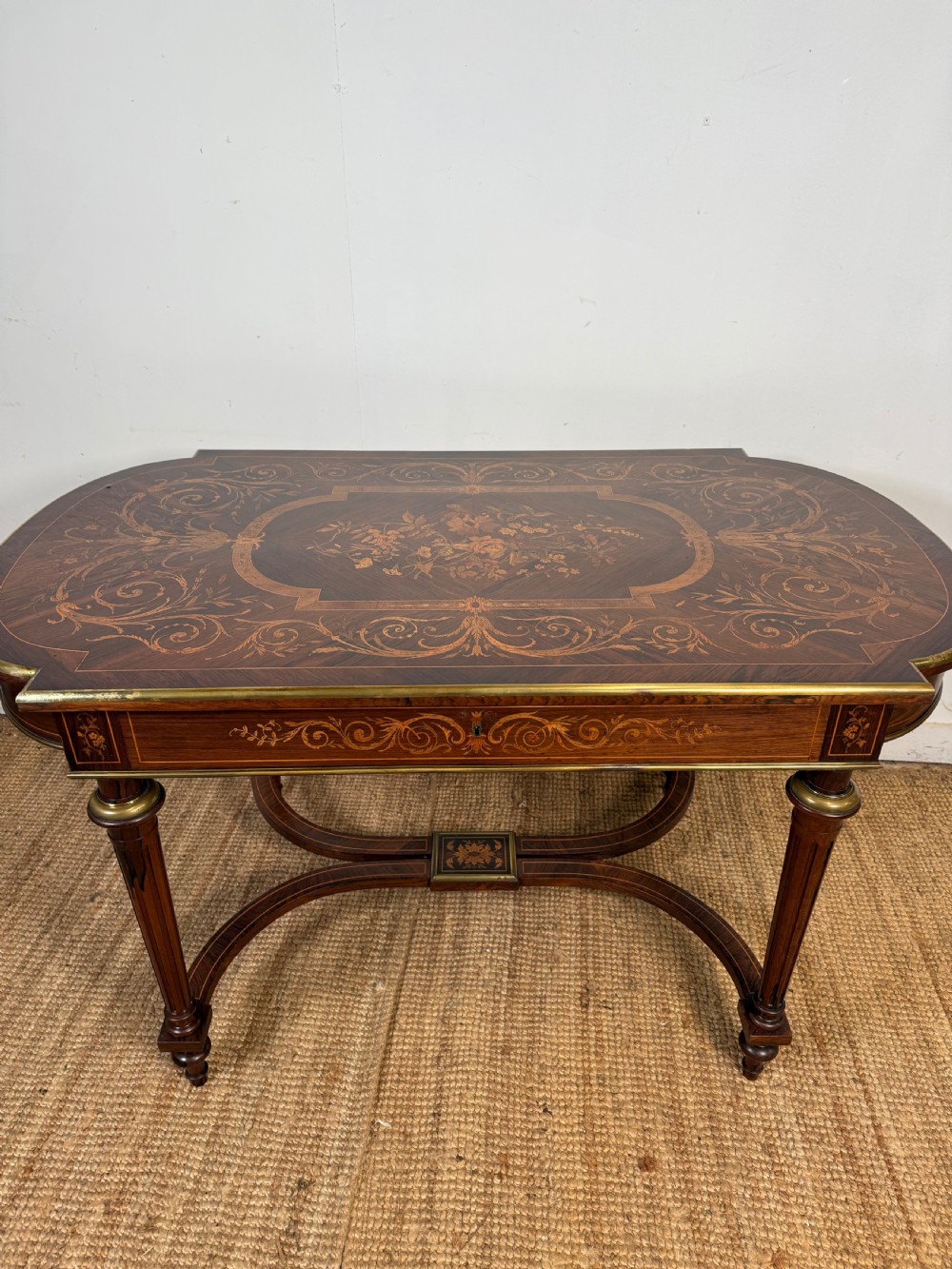 A French Napoleon III period centre table featuring floral wood marquetry, brass edges, tapered fluted legs, and an arched lower stretcher. View V