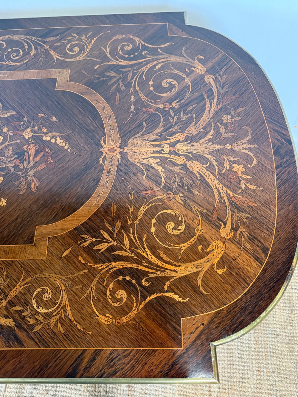 A French Napoleon III period centre table featuring floral wood marquetry, brass edges, tapered fluted legs, and an arched lower stretcher. View VIII