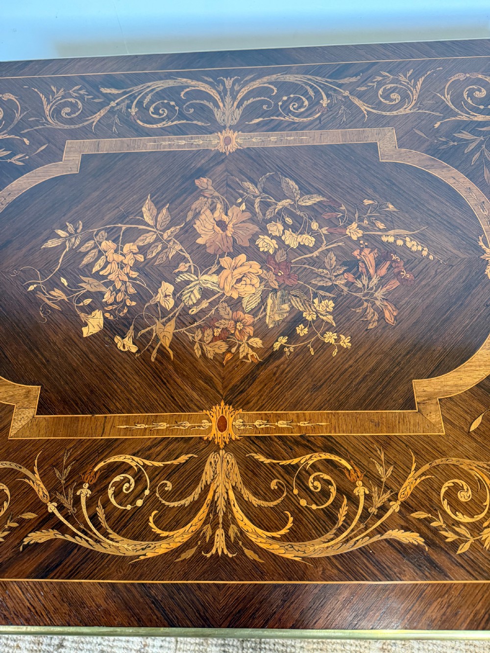 A French Napoleon III period centre table featuring floral wood marquetry, brass edges, tapered fluted legs, and an arched lower stretcher. View IX