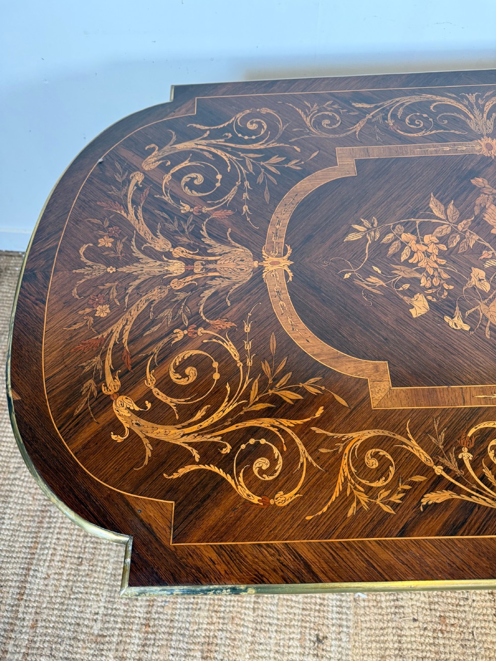 A French Napoleon III period centre table featuring floral wood marquetry, brass edges, tapered fluted legs, and an arched lower stretcher. View X