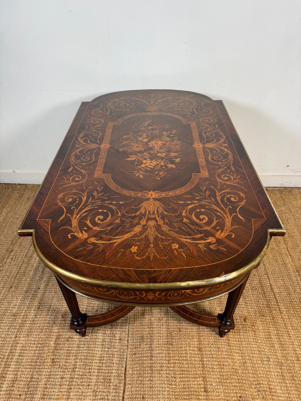 A French Napoleon III period centre table featuring floral wood marquetry, brass edges, tapered fluted legs, and an arched lower stretcher. View XI
