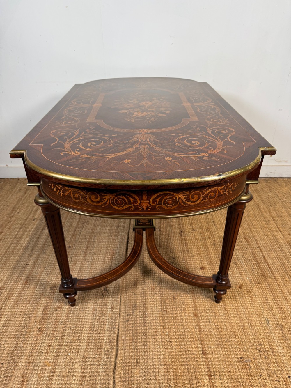 A French Napoleon III period centre table featuring floral wood marquetry, brass edges, tapered fluted legs, and an arched lower stretcher. View XII
