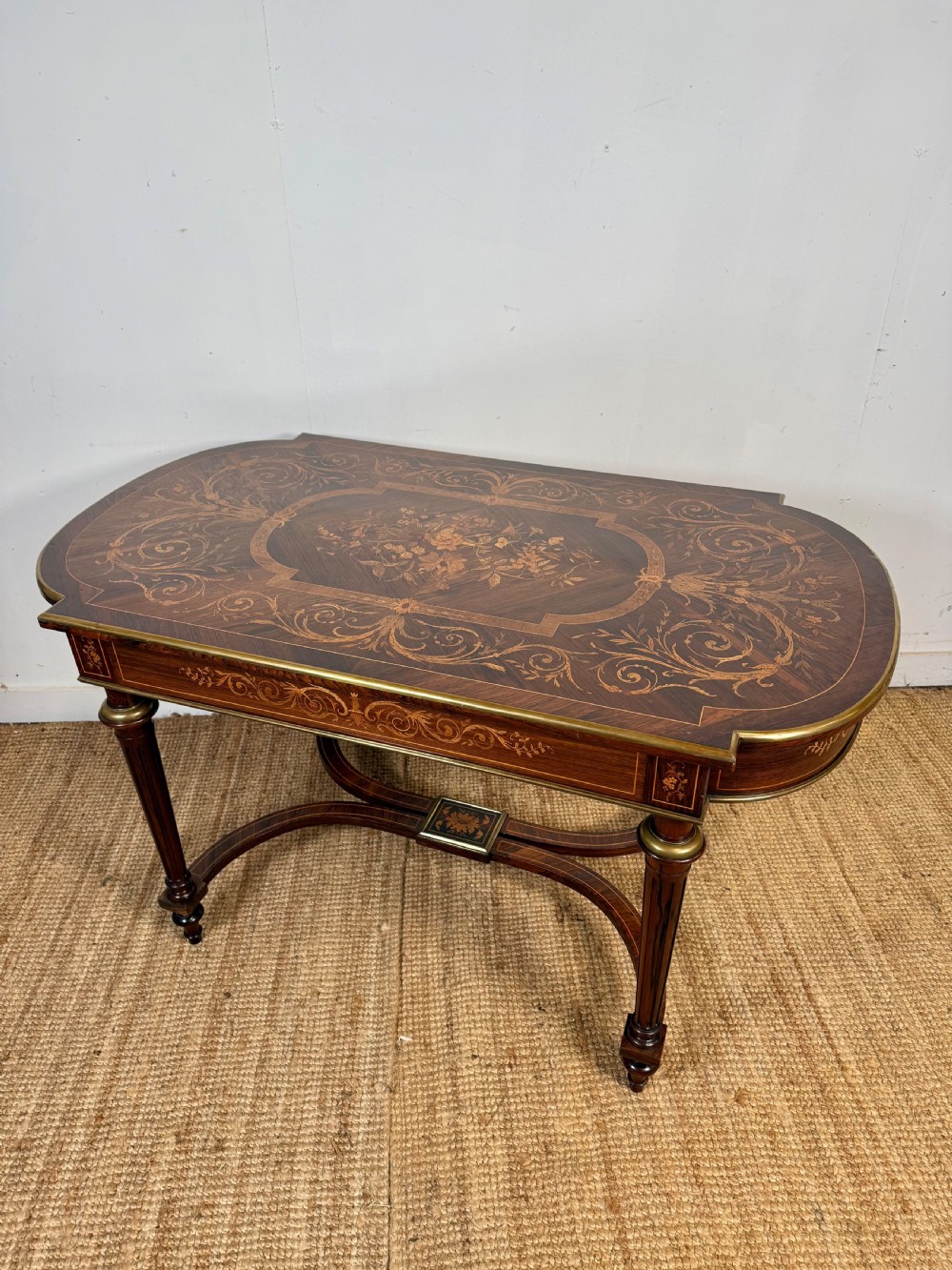 A French Napoleon III period centre table featuring floral wood marquetry, brass edges, tapered fluted legs, and an arched lower stretcher. View XIII