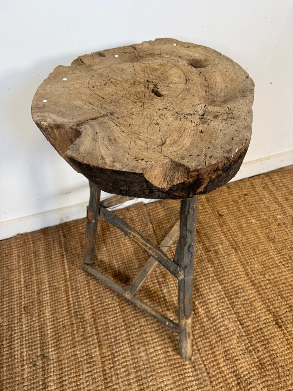 A rustic timber chopping block featuring a thick round log cross-section top supported by three weathered wooden legs with a wire mesh shelf. View II