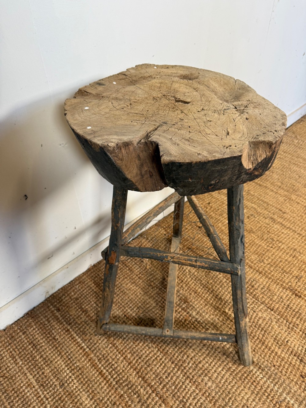 A rustic timber chopping block featuring a thick round log cross-section top supported by three weathered wooden legs with a wire mesh shelf. View III