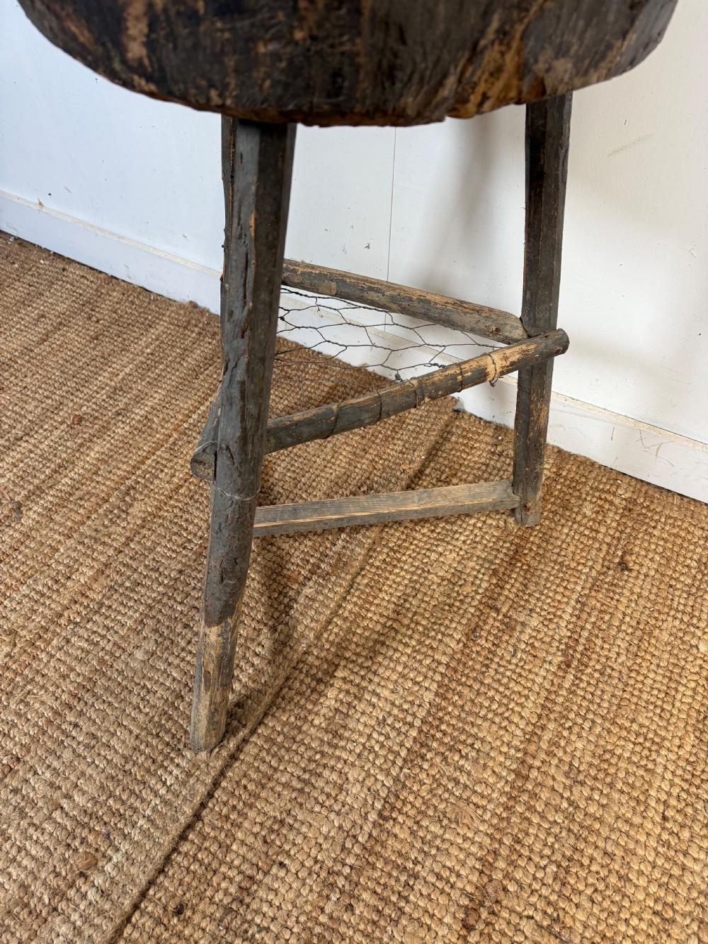 A rustic timber chopping block featuring a thick round log cross-section top supported by three weathered wooden legs with a wire mesh shelf. View VI