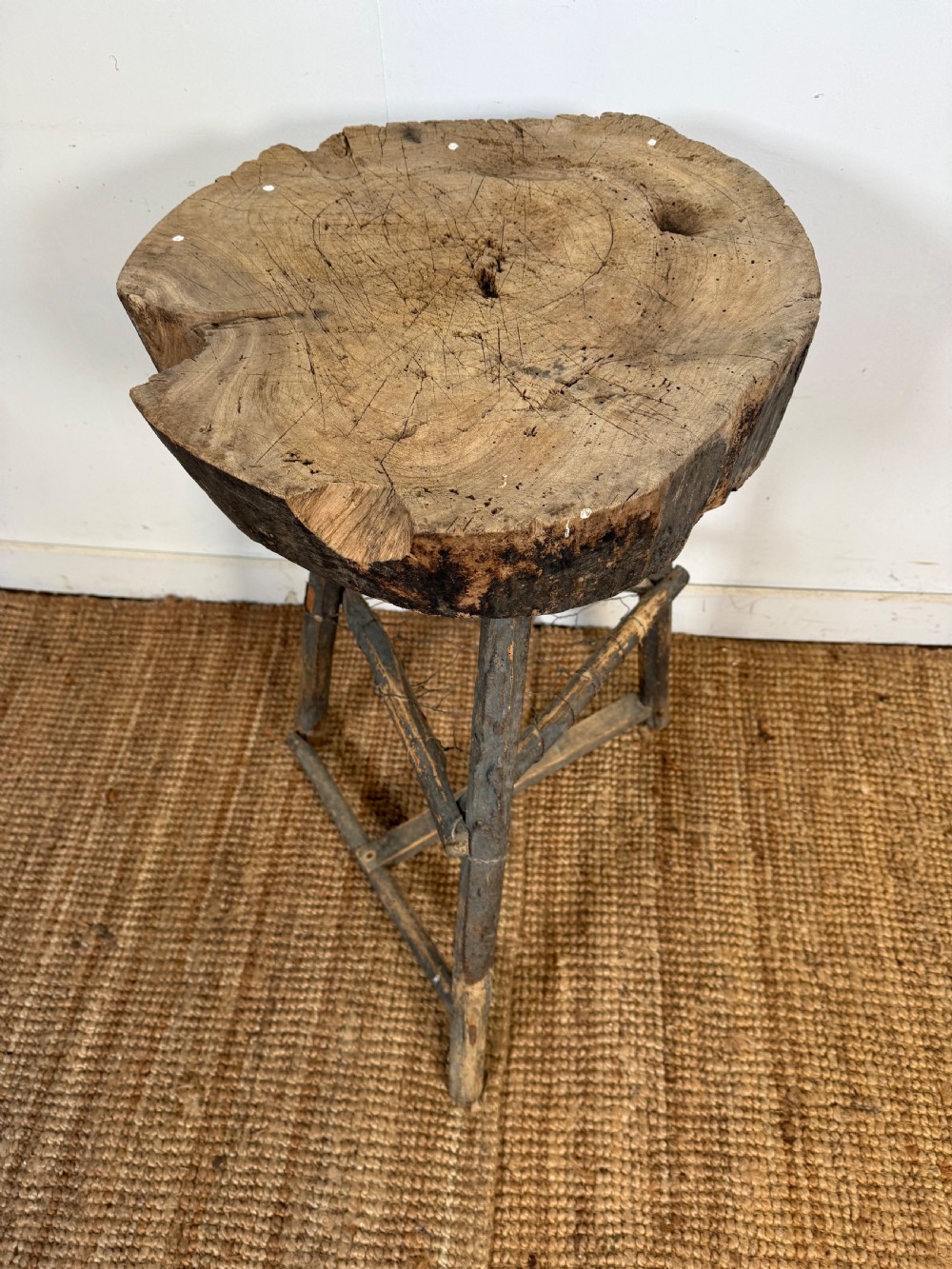 A rustic timber chopping block featuring a thick round log cross-section top supported by three weathered wooden legs with a wire mesh shelf. View VII