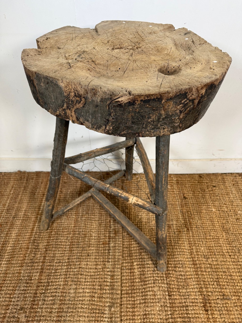 A rustic timber chopping block featuring a thick round log cross-section top supported by three weathered wooden legs with a wire mesh shelf. View VIII
