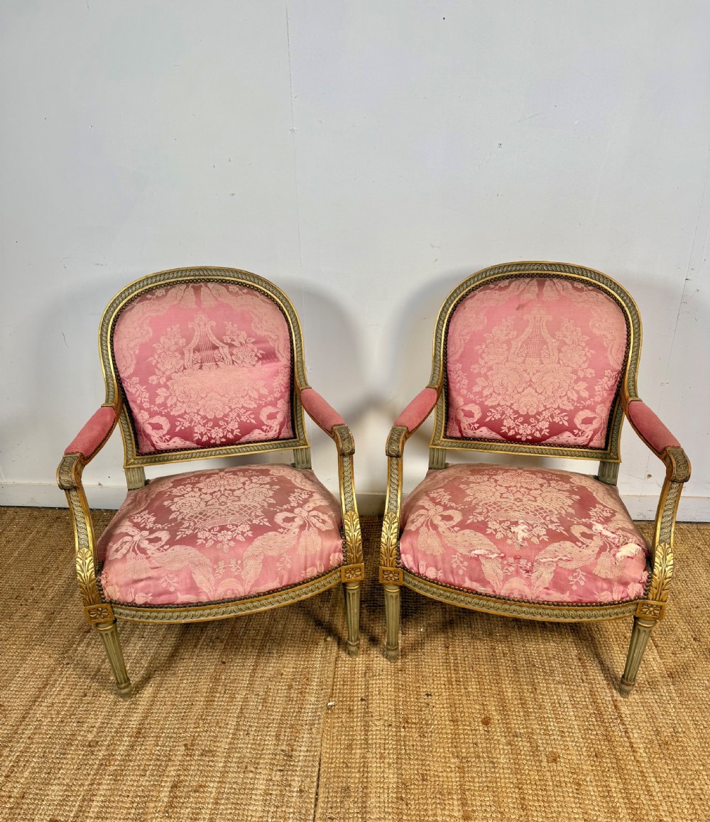 A pair of Louis XVI style French open armchairs featuring carved giltwood frames, fluted legs, and pink damask pattern upholstery.