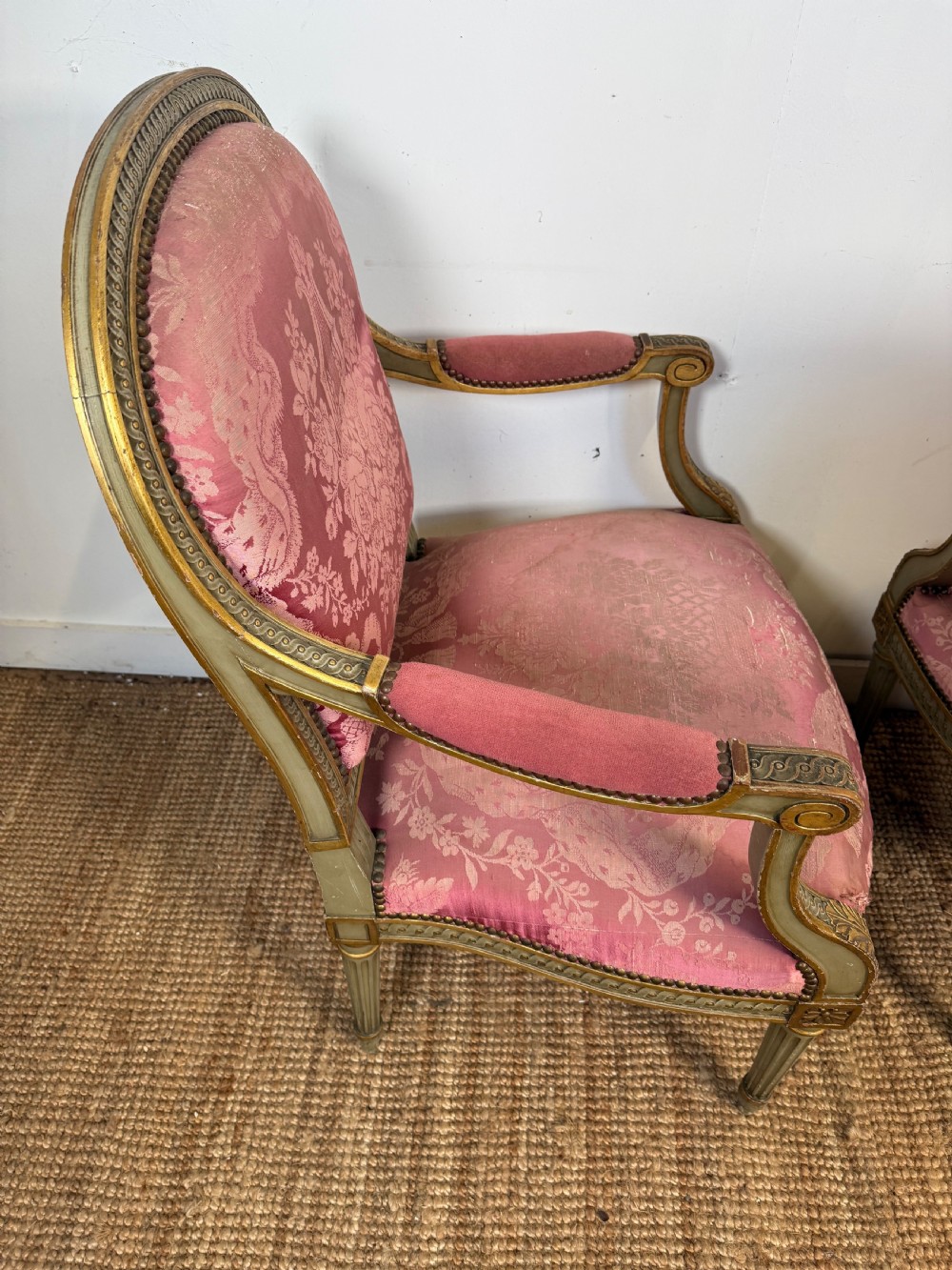 A pair of Louis XVI style French open armchairs featuring carved giltwood frames, fluted legs, and pink damask pattern upholstery. View X