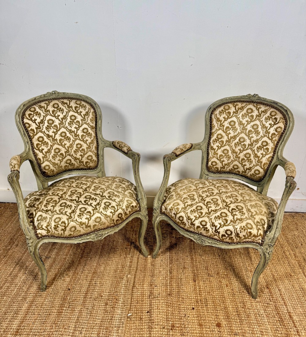 A pair of late 19th-century French style open armchairs with carved muted green painted frames and patterned velvet fabric.