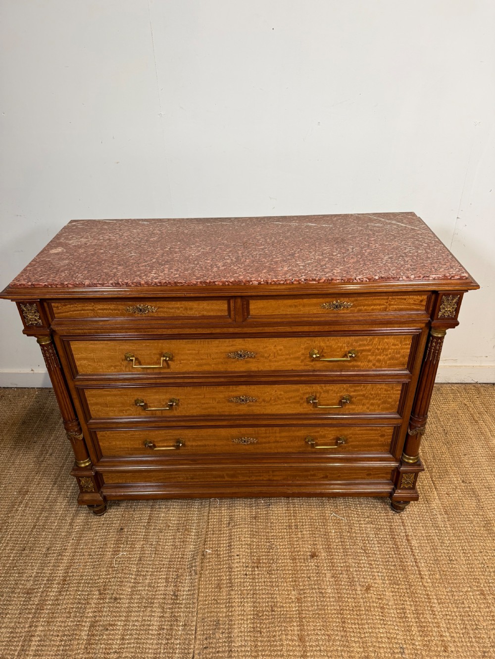 A 19th-century French mahogany commode featuring a red marble top, brass drop handles, and fluted corner columns.